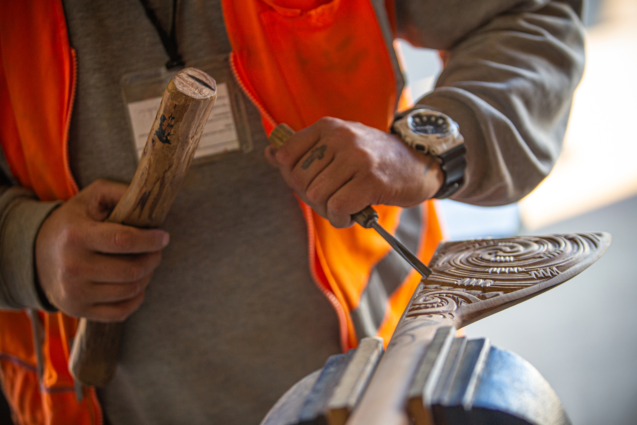 Man in prison works away at carving an intricate pattern into wood