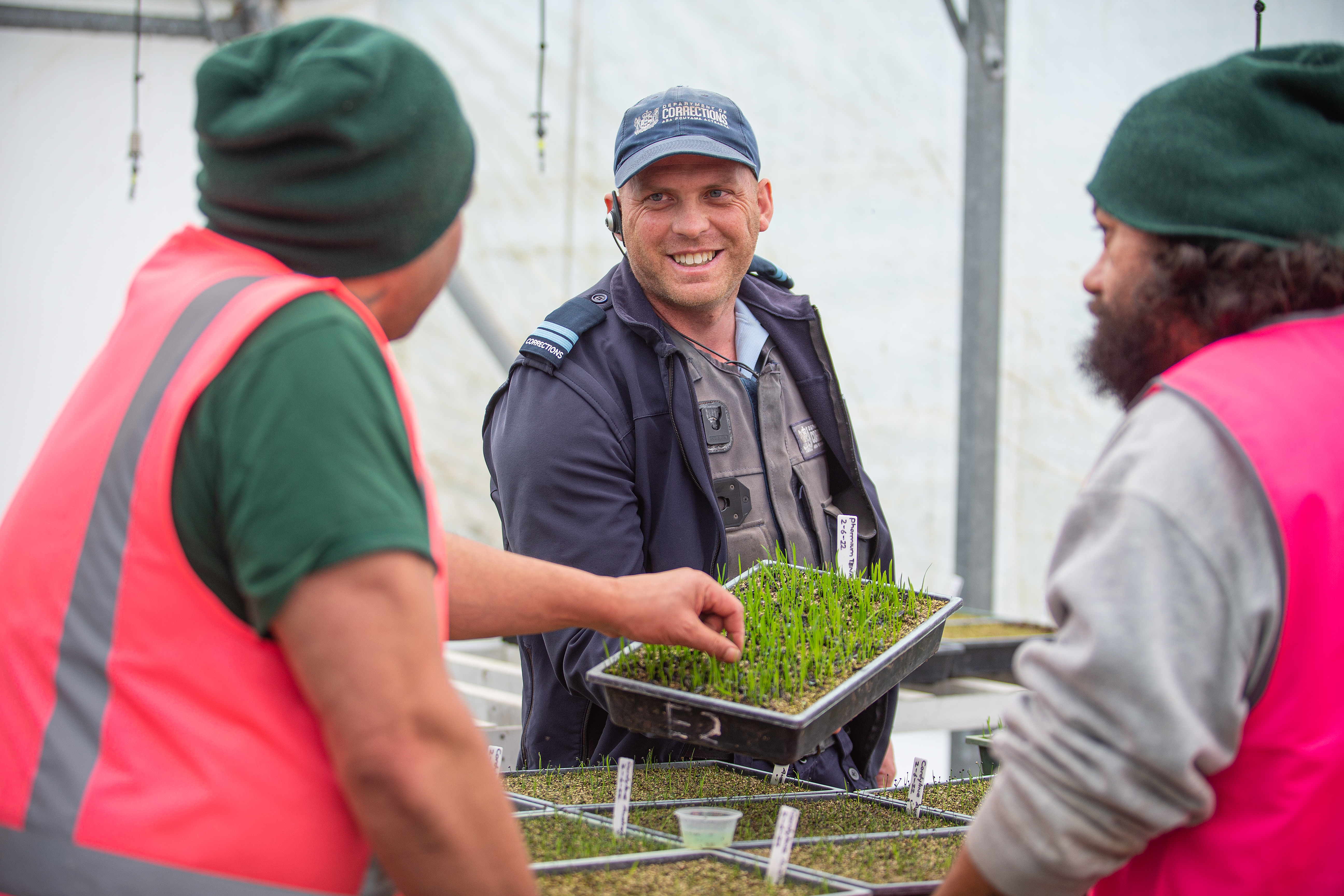 Horitculture istructor holds punnet of growing grass out to two men taking part in industry training